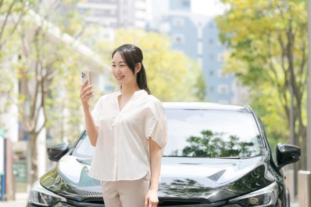 車の前でスマホを操作する女性