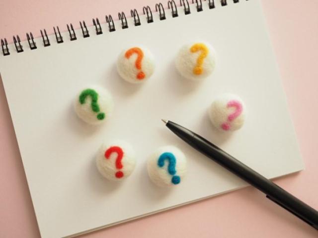 ノートに書かれた複数のクエスチョンマークとペン