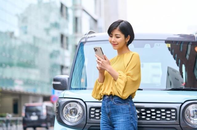軽自動車の前でスマホを触る女性