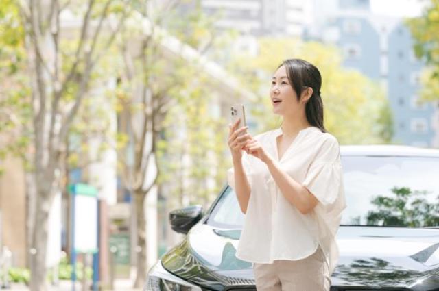 車の前でスマホを操作する女性