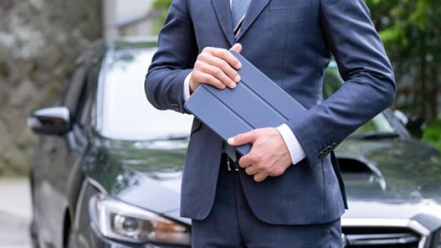 タブレットを持って車の前に立つビジネスパーソン