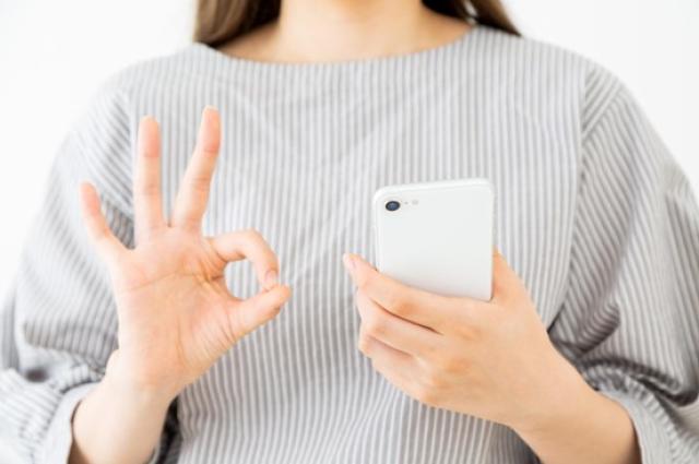 スマホを手にOKサインを出す女性