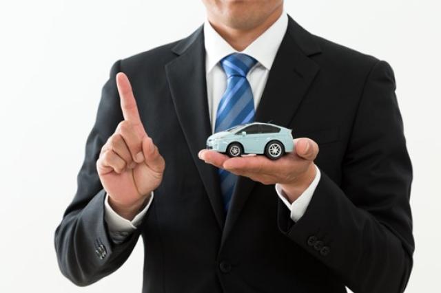 ミニカーを左手に載せ右手の人さし指を立てるスーツ姿の男性