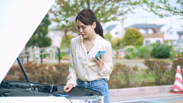 スマホを片手にエンジンルームを見る女性