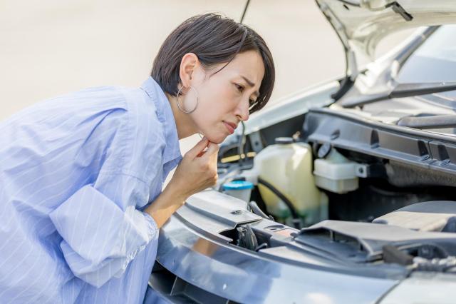 車のエンジンルームを覗き込んで考える女性