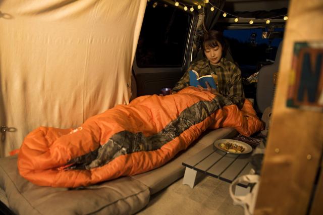 マットの上に寝袋を敷き車中泊を楽しむ女性