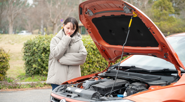 車のボンネットを開けて困った顔で見つめる若い女性