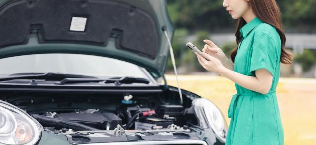 車のボンネットを見ながらスマホを操作する女性