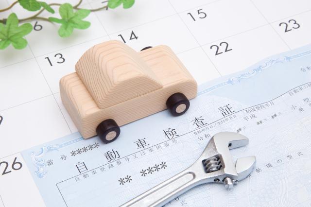 カレンダーの上に置かれた木製の車と車検証と工具
