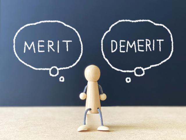 メリットとデメリットの文字を思い浮かべる木製の人形