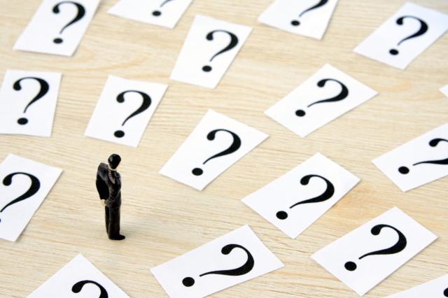 クエスチョンマークが書かれたカードを眺める人形